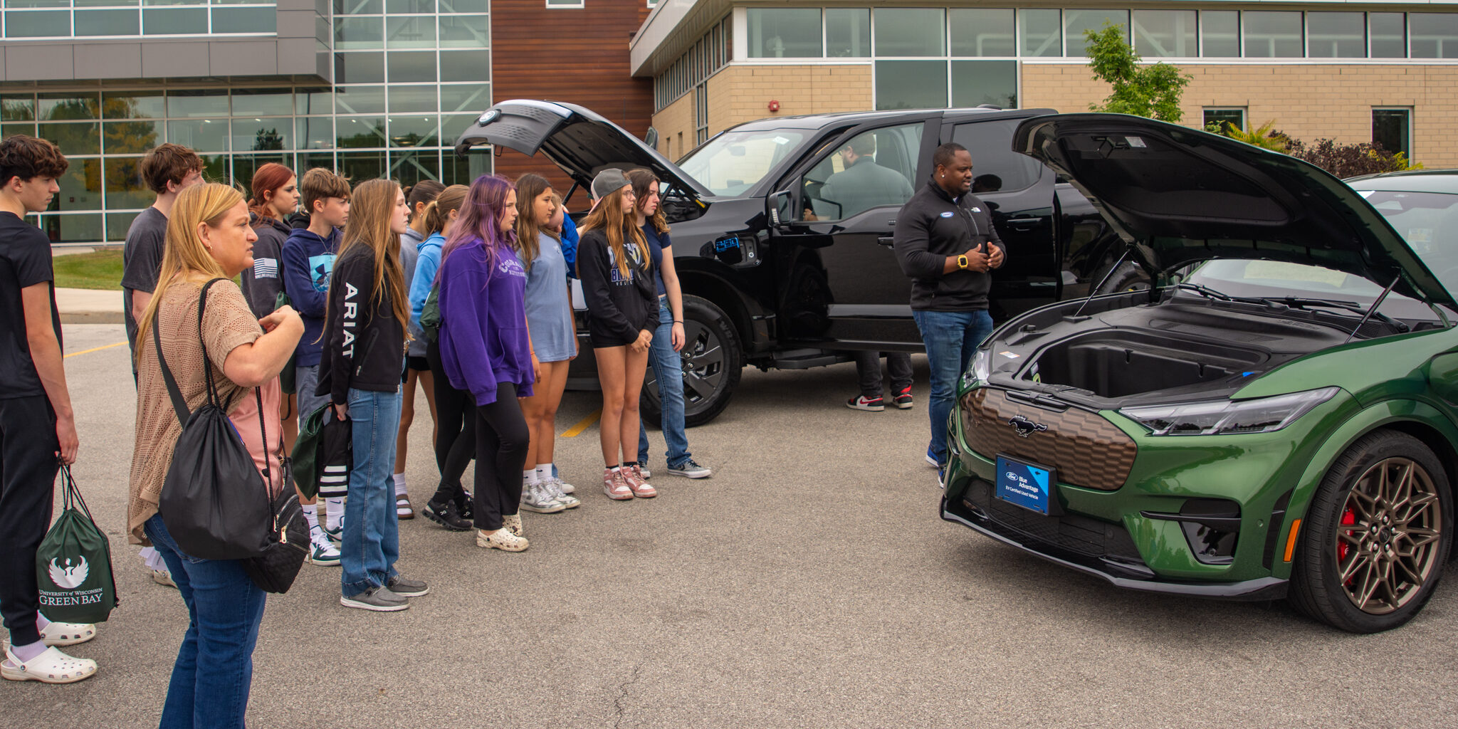A group of high school students listens to a car salesman discuss how electric vehicles operate.