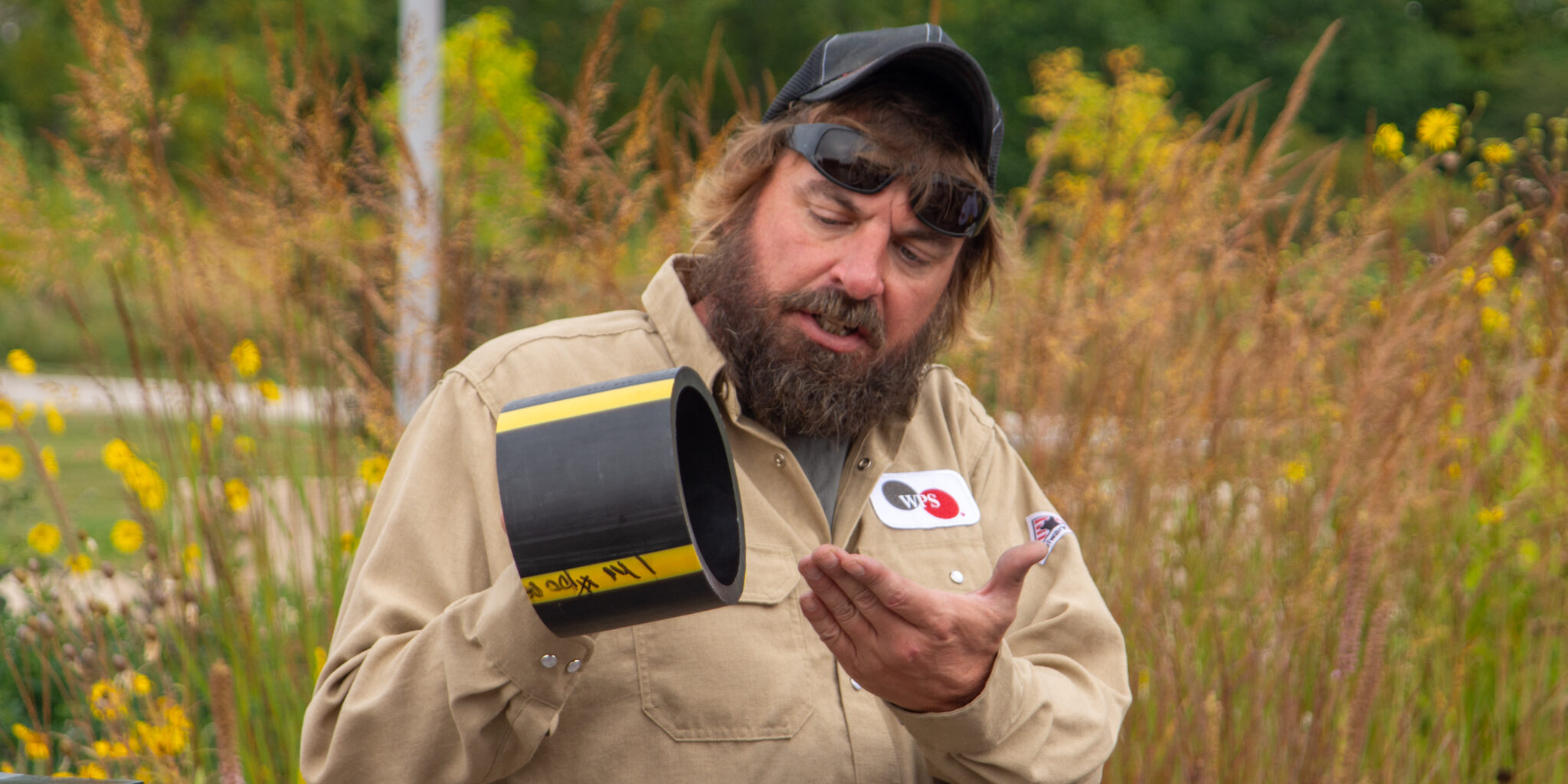 A WPS employee holds up a section of black and yellow natural gas piping.