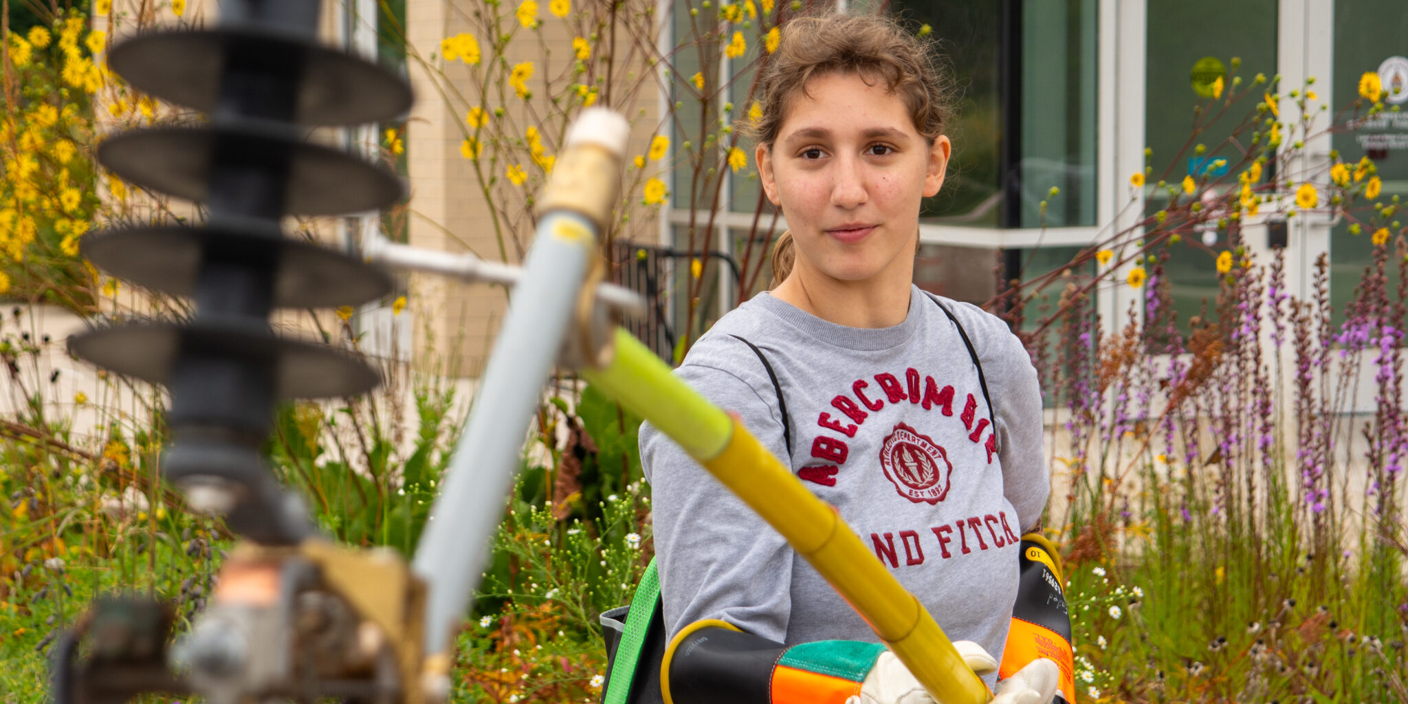 A high school student uses a long yellow stick to attach a mock electric fuse.