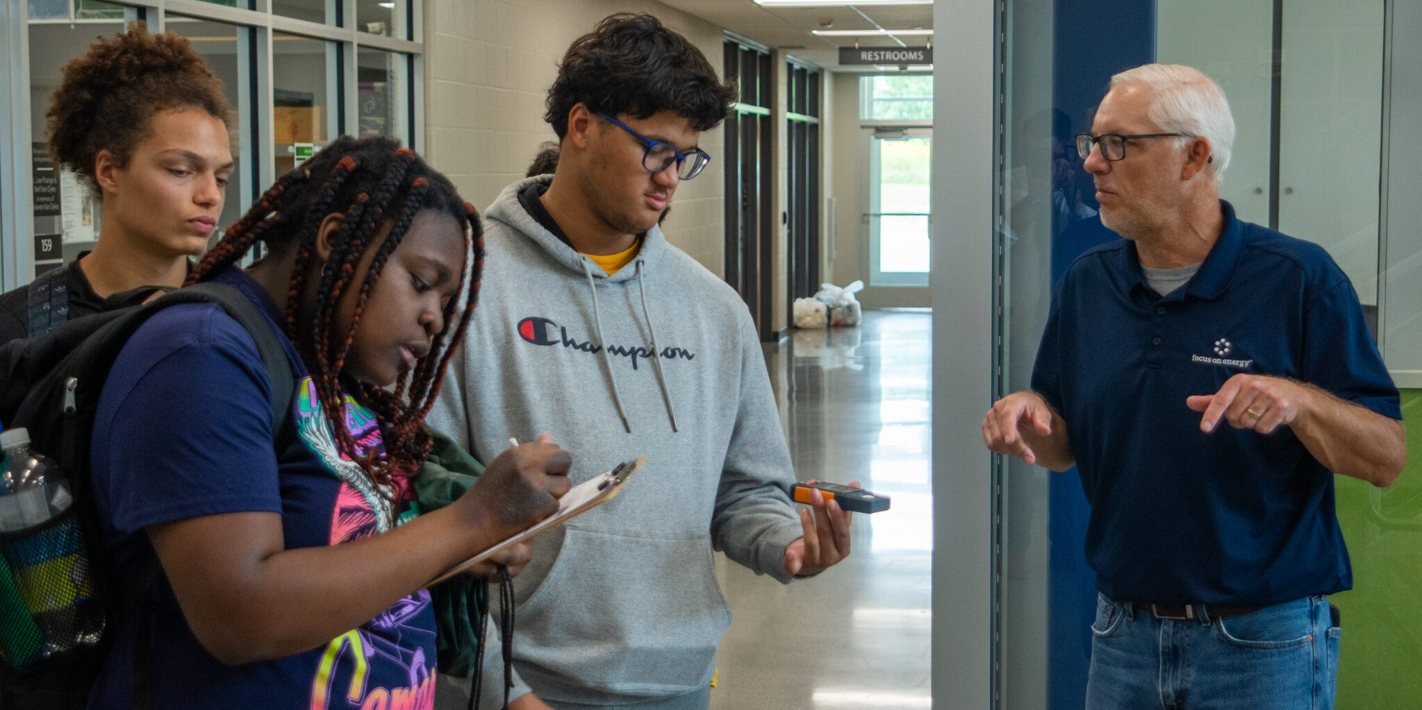 A group of high school students and an instructor measure air temperature inside a large building.