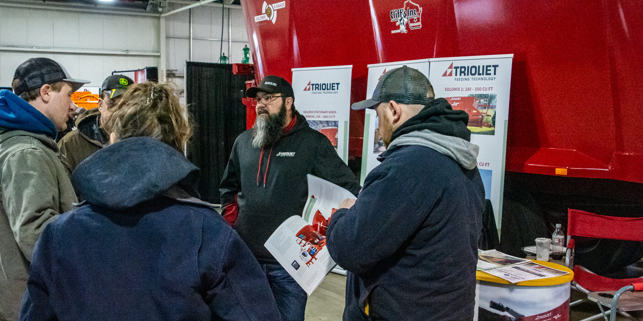 An exhibitor talks with visitors near a large red piece of farm machinery at the WPS Farm Show.