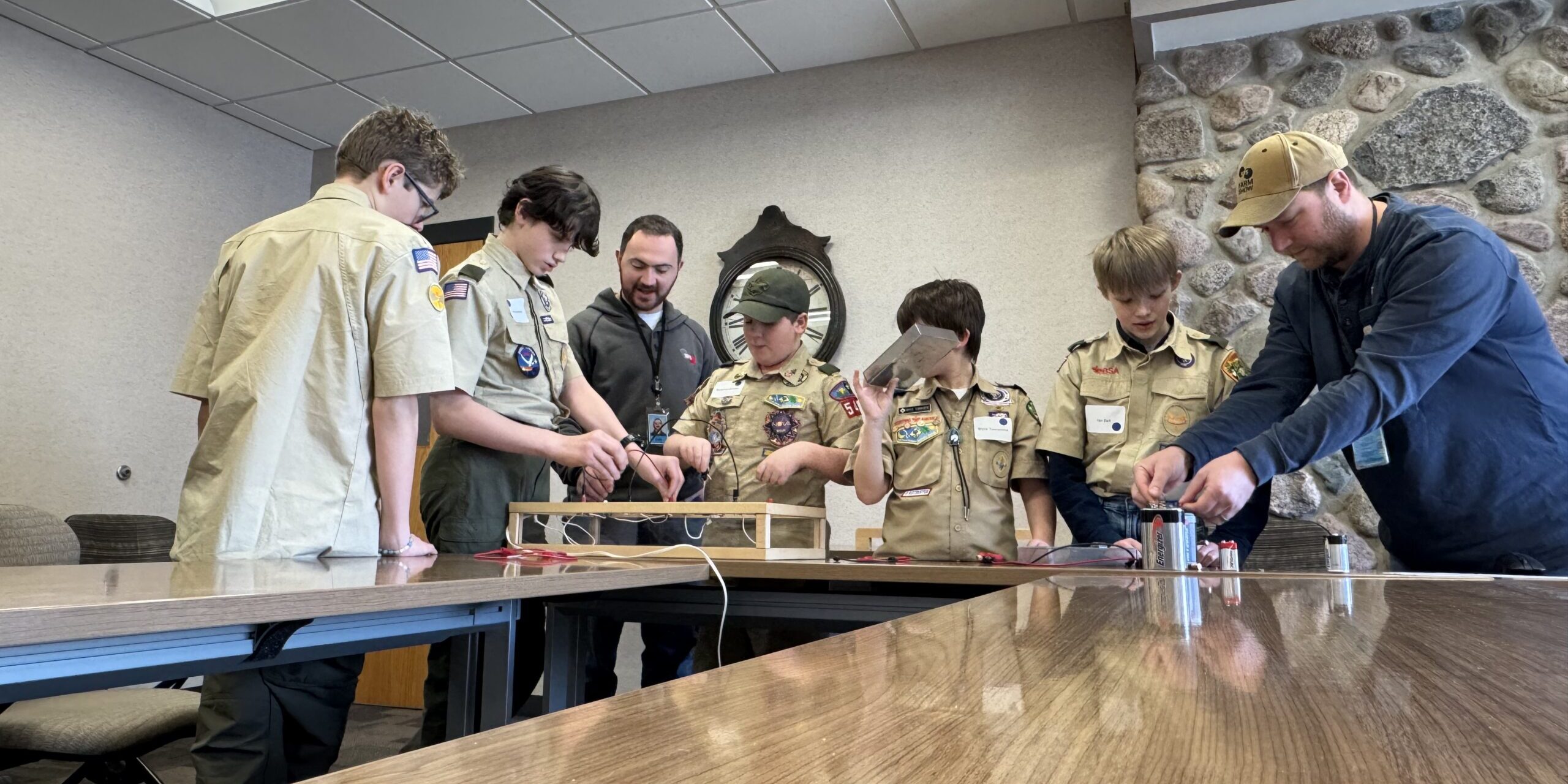 A small group of Scouts connects simulated electric circuits together on tabletop displays in a conference room.