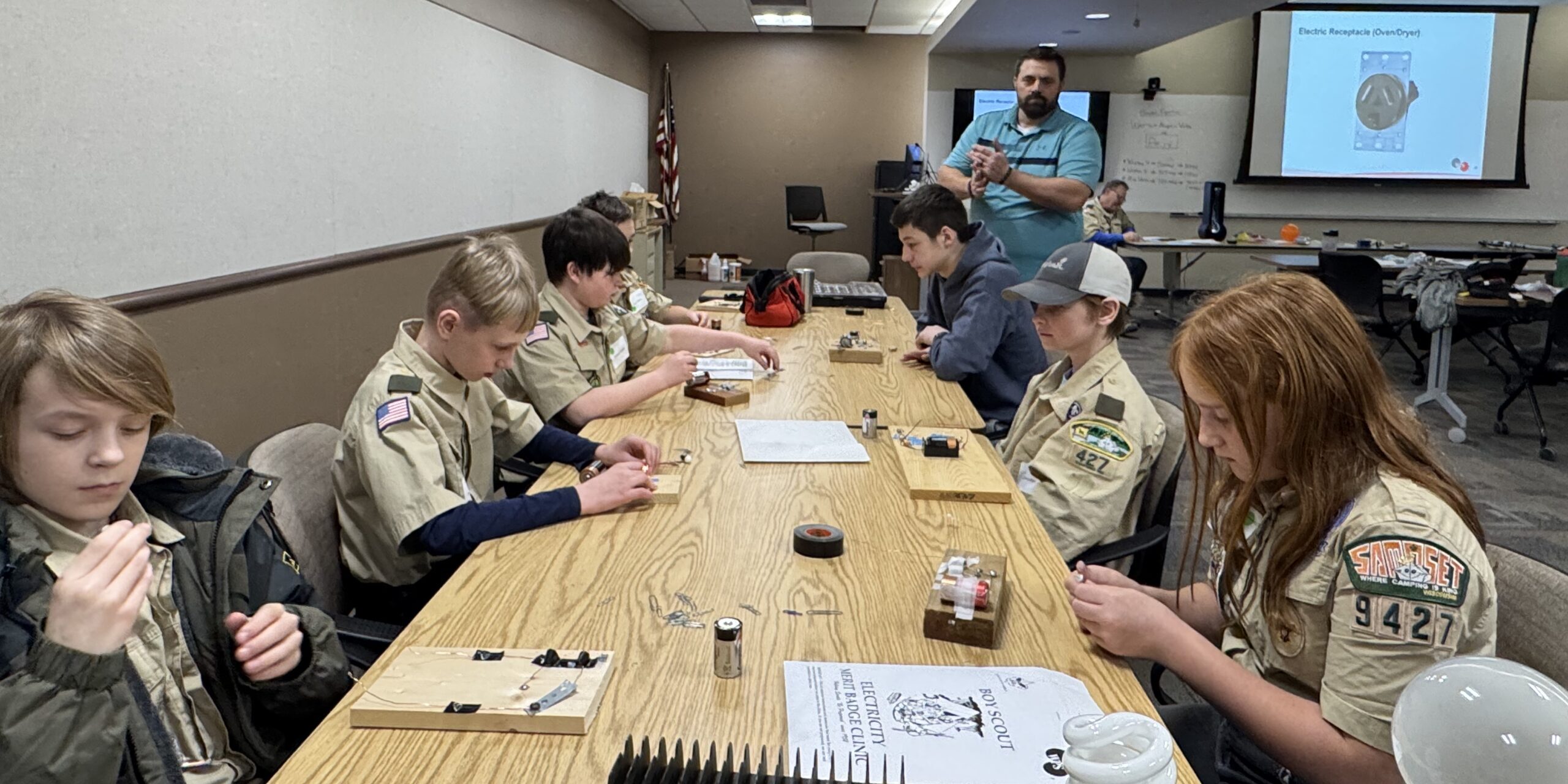 A group of Scouts sitting at a conference table assemble small electric circuits powered by batteries.