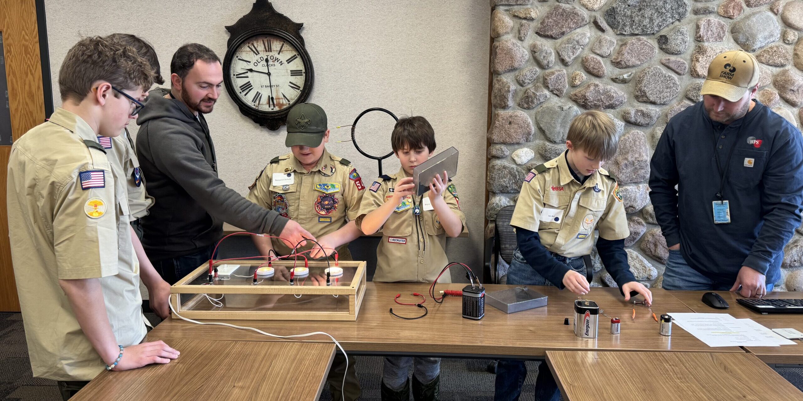 Two WPS employees help teach a small group of Scouts how to create electric circuits in a conference room.