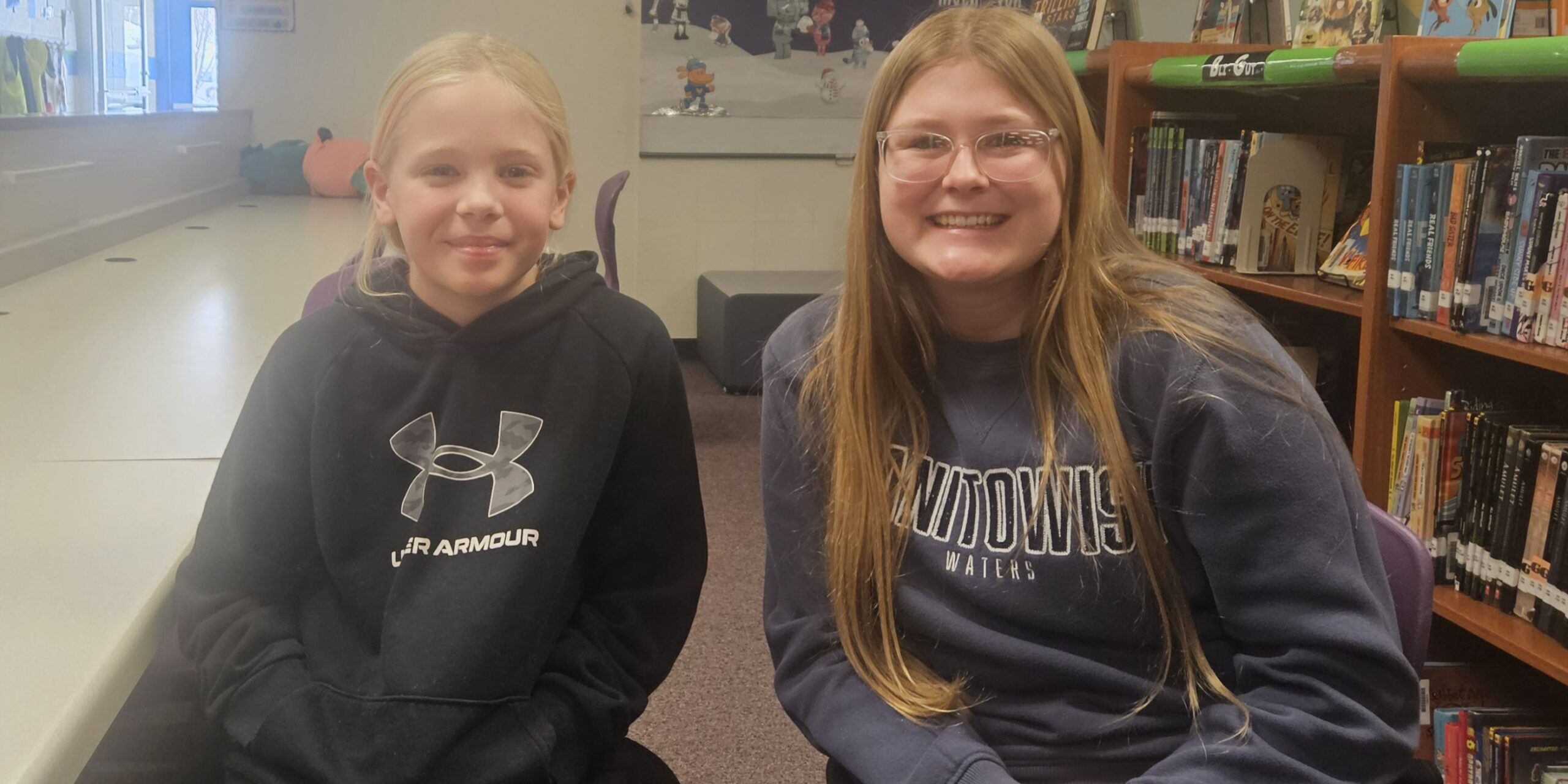 A woman and a girl smile for a photo while sitting at a table in a library