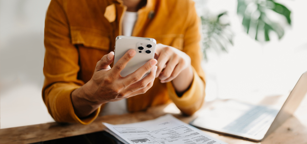 A close-up photo of a woman using an iPhone while at a table with a bill on it.