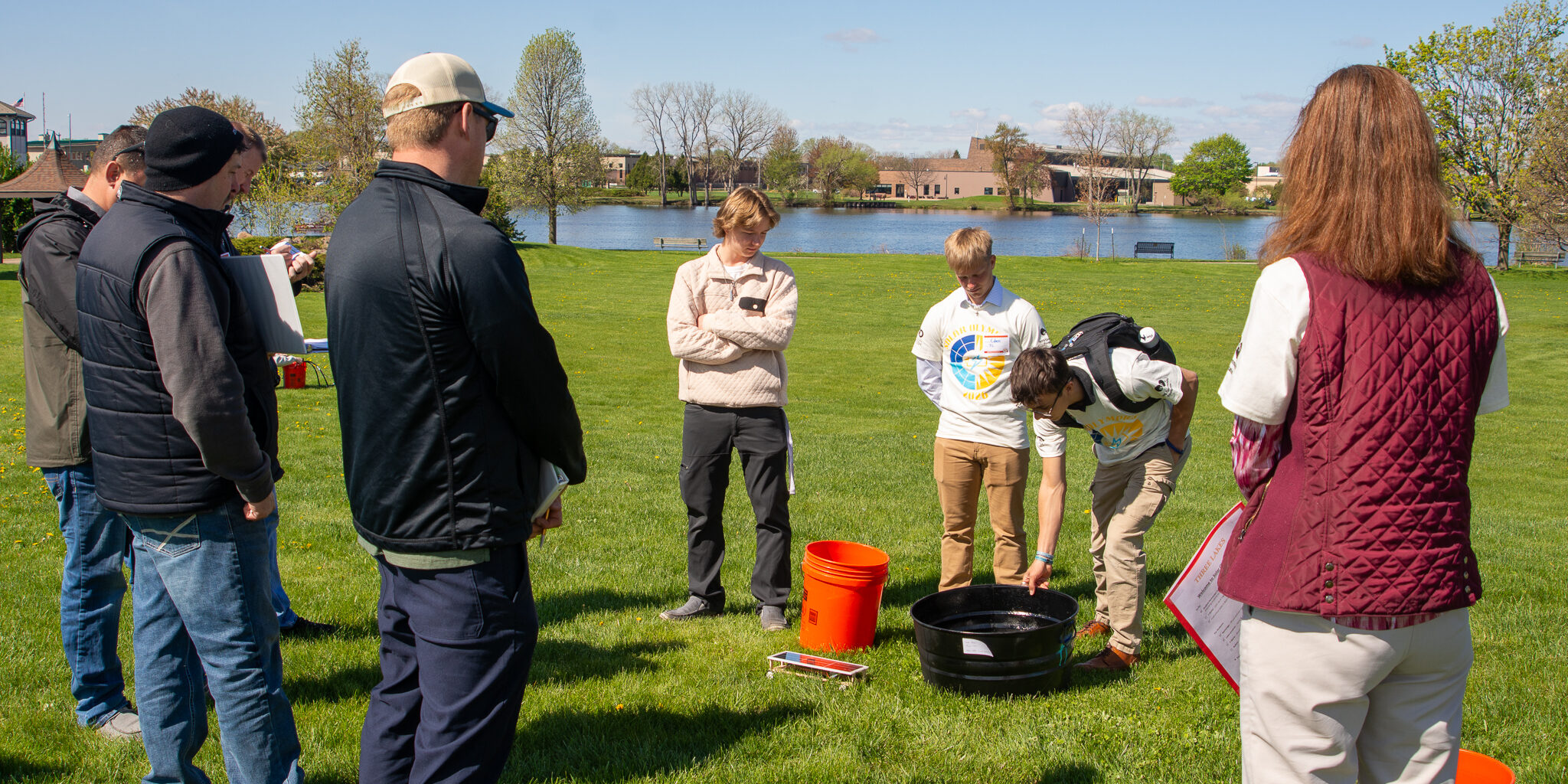 A group of event judges listens to a three male high school students discuss a solar water heater project at the 30th annual WPS Solar Olympics.