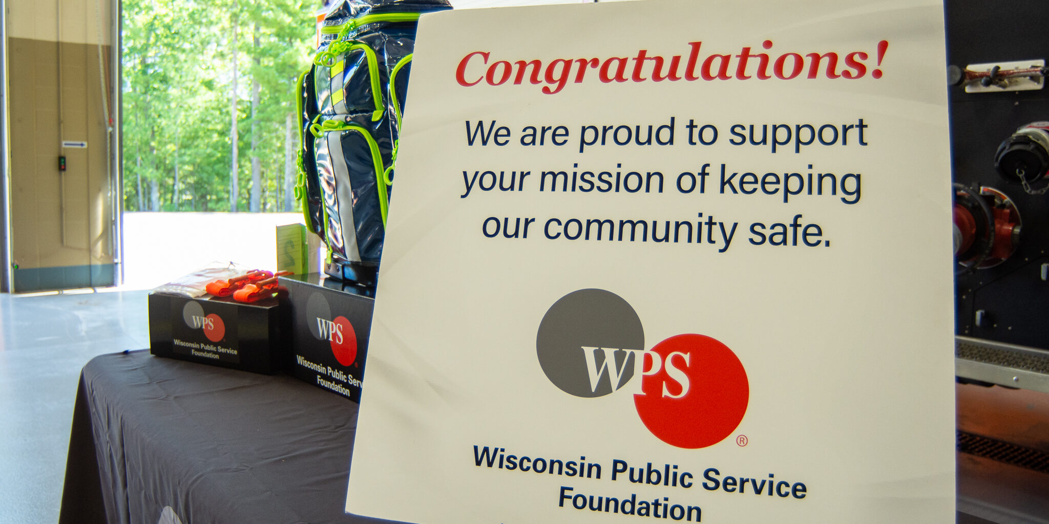 A congratulatory sign from the WPS Foundation in front of emergency medical supplies arranged on a table. The sign text reads, "Congratulations! We are proud to support your mission of keeping our community safe."