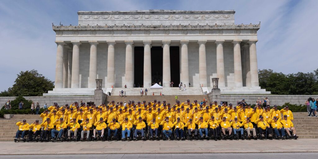 A large group of military veterans wearing yellow shirts standing or sitting in front of the Lincoln Memorial.