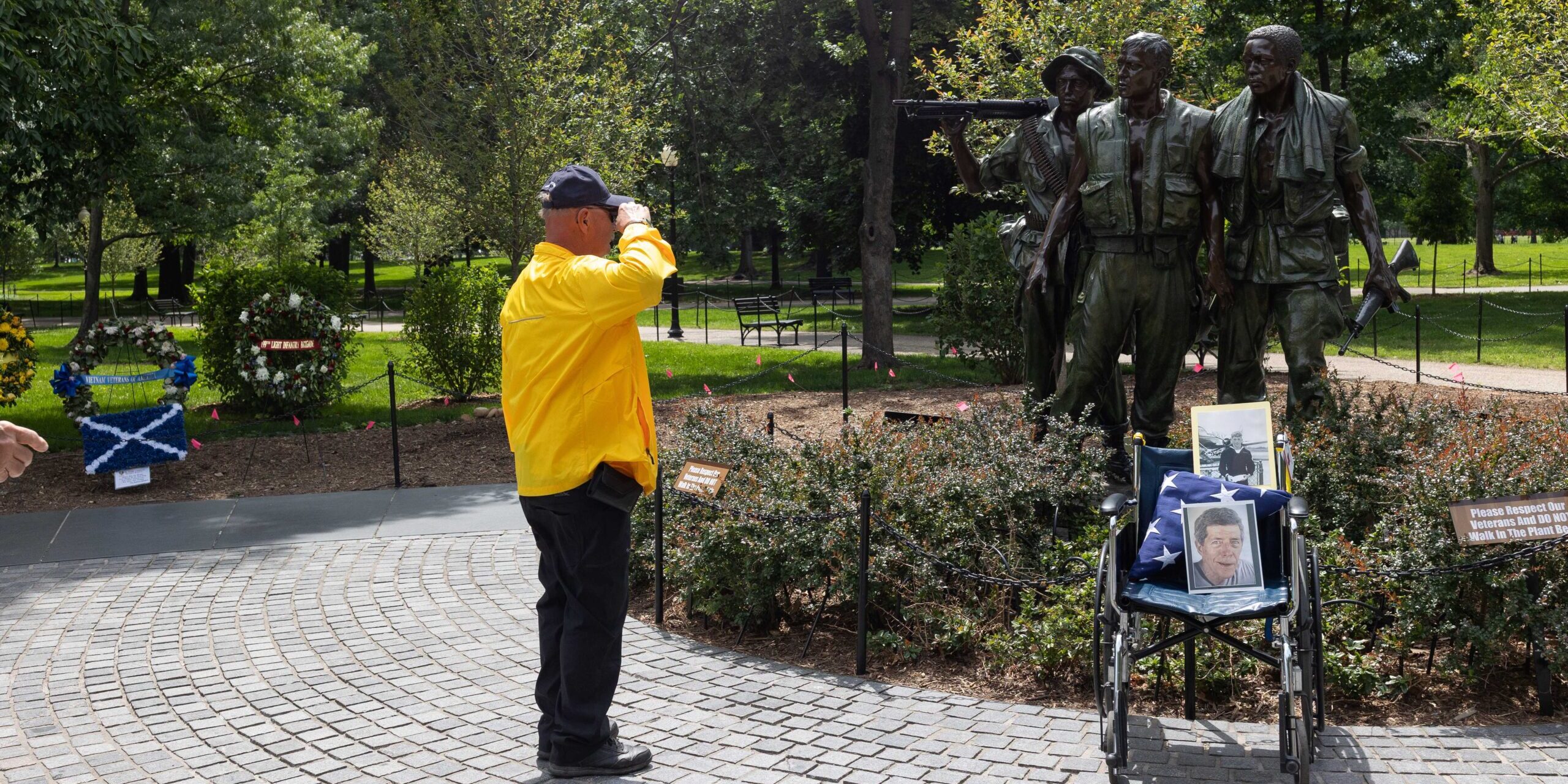 A military veteran in a yellow coat salutes statues of soldiers at the Vietnam War Memorial.