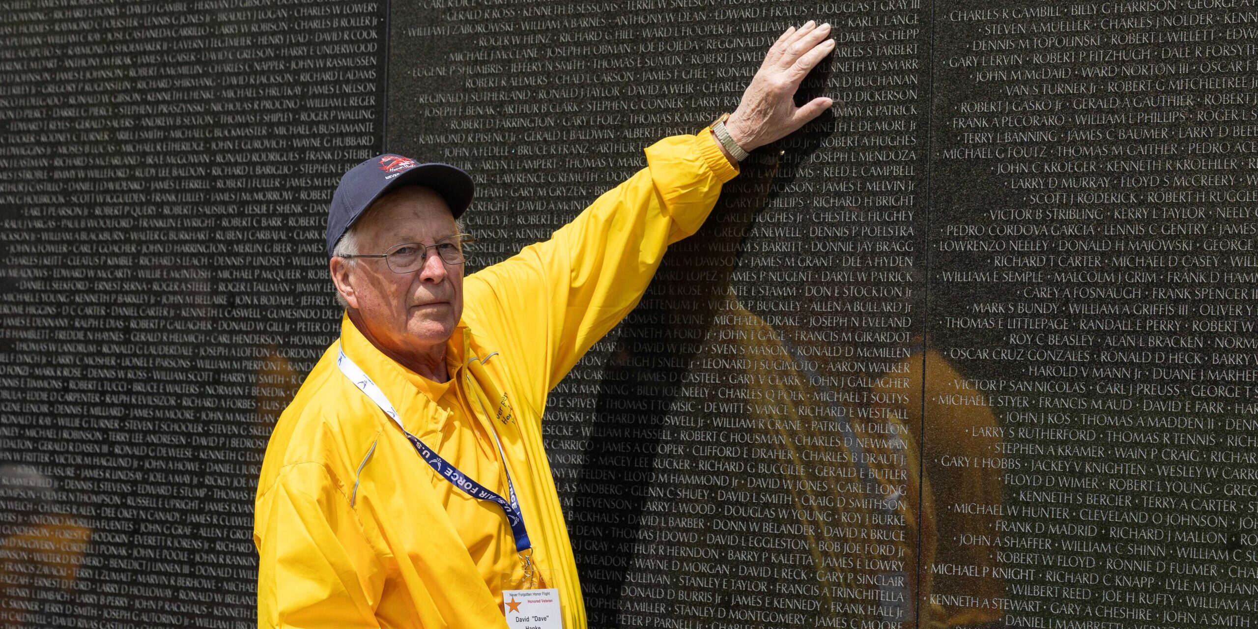 A military veteran wearing a yellow coat touches names engraved into the Vietnam War Memorial