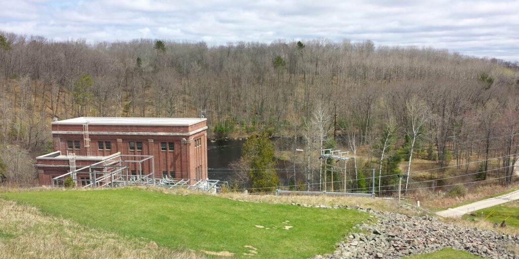 A photograph of a hydroelectric dam set into the side of a hill above a small lake.