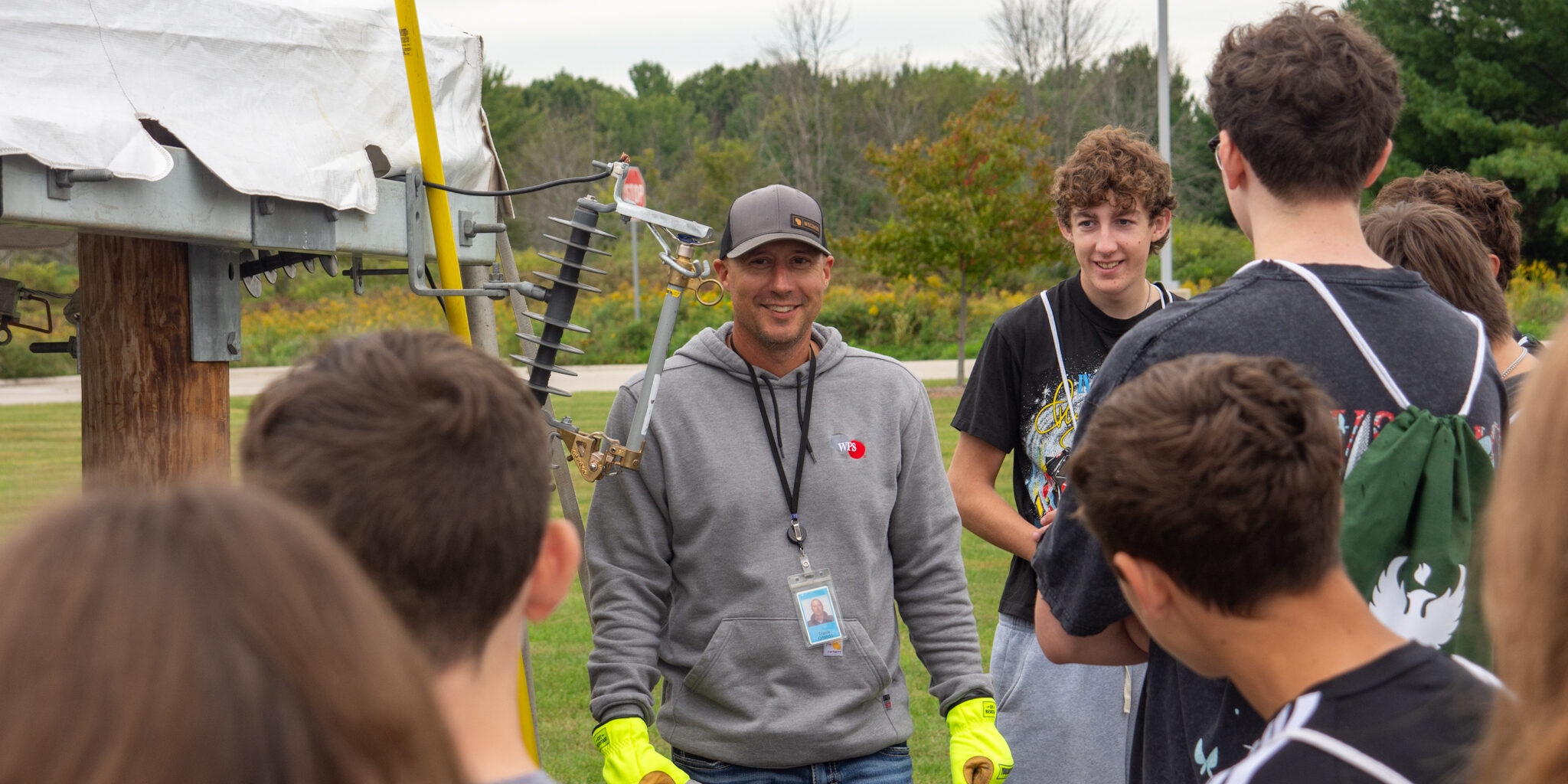A WPS employee smiles while speaking with a group of high school students near a mock wiring display.