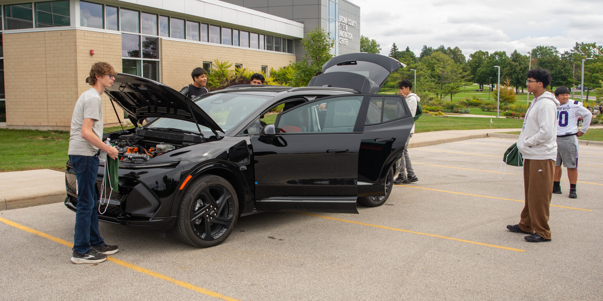 A small group of high school students look at and study a black SUV-style electric vehicle.